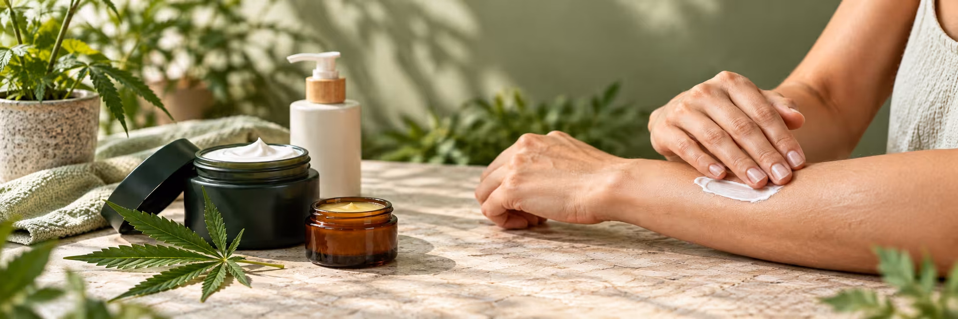 What Are Cannabis Topicals? How They Work Person applying cannabis topical cream to their forearm beside cream and balm jars and a cannabis leaf.